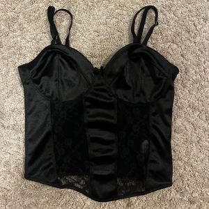 Svart satintopp - Säljer denna svarta korsettliknande satintopp från H&M. Säljs då den inte kommer till användning. Den har även spets framtill. Är i nyskick då den sällan användts!!
