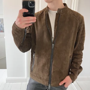 Hugo boss jacka  - Hugo boss jacka, väldigt rare Hugo boss jacka som är liksom mocka matieral. Vet ej till tusen procent om det är exakt mocka dock. Kolla gärna taggen, tror man kan hitta exakta modellen så kan man få reda på fler detaljer om jackan. Den är väldigt skön och sitter najs med dubbel kedjad och en väldigt najs logga på ärmen. Modellen är 180 cm 75 kg och bär L. Kom med frågor! 