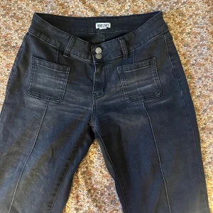 Svarta bootcut jeans från Madlady - Snygga svarta jeans från Madlady med bootcut passform och medel midja. Jeansen har framfickor med markerade sömmar, dubbla knappar i midjan och bakfickor med lock och knapp. Materialet är stretchigt jeans för en bekväm känsla. Storlek 38/short 