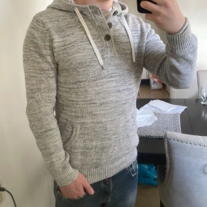 Grå unik stickad hoodie - Riktigt snygg grå dtickad hoodie med knappar upp vid kragen. Storlek XS men passar mer som S. Modellen är 180cm, 73kg. Priset går att diskutera!