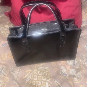 Svart glansig handväska  - Snygg glansig svart handväska! Långt band ingår också! Knappt använd. 