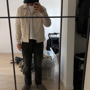 Beige jeansjacka med knappar - Säljer en stilren beige jeansjacka med klassisk krage och knäppning framtill. Jackan har två bröstfickor med lock och knappar samt raka ärmar. Perfekt för dig som vill ha en clean och enkel look.