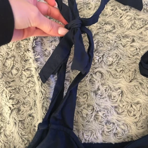 Marinblå klänning Holly & Whyte S - Enkel marinblå klänning från Holly & Whyte by Lindex i storlek S. Klänningen har smala axelband som knyts med rosett på axlarna och rak passform. Perfekt för varma dagar och lätt att styla med accessoarer.