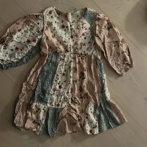 Blommig klänning, Zara kids  - Supersöt klänning  i storlek 128 (8år). Klänningen har ett patchworkmönster med blommor och prickar i pastelliga toner av rosa, vitt och grönt. Långa puffärmar, knappar framtill och volangkant nertill. Knappt använd 