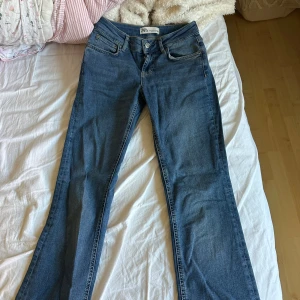 Blå bootcut jeans från Zara, stl 34 - Snygga blå jeans från Zara i storlek 34 med klassisk femficksdesign och bootcut-ben. Jeansen har normal midja och är tillverkade i mjukt denimtyg som ger en skön passform. Perfekta för dig som gillar en tidlös och trendig look.