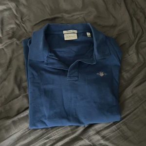 Blå pikétröja från GANT Regular Fit - Snygg blå pikétröja från GANT i storlek S med klassisk krage och knappslå. Regular fit för en skön och avslappnad passform. Tröjan har GANT-logga broderad på bröstet och är tillverkad i mjuk bomull som andas. Perfekt för dig som gillar stilrena och tidlösa plagg. Pris kan diskuteras 