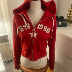 Cropped zip up hoodie röd - Röd cropped zip up hoodie med tryck (ish) och stor luva! Från BDG köpt från Urban outfitters i Spanien. Väl använd men inga täcken på dåligt skick. Mycket bekväm i storleken Large. Köpt för 500kr på plats.