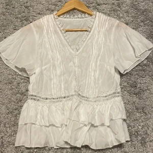Vit topp  - Säljer denna fina halvätnas toppen som jag aldrig använt men den är lite skrynklig. Det ska nog gå bra att stryka den.  Den har fina detaljer. Säljer den för 50 kr.