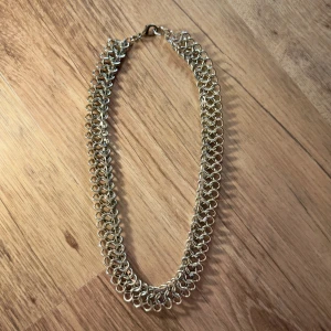 Bred kedjehalsband i guldton - Unikt halsband med bred kedjedesign i guldton. Halsbandet består av tätt sammanlänkade ringar som ger ett coolt och robust intryck. Perfekt för dig som vill sticka ut med ett statement-smycke. Stängs med karbinhake.