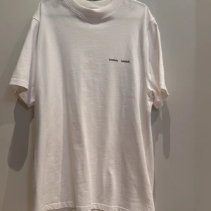Vit t-shirt från Samse Samse - Vit t-shirt från Samse Samse med enkel design och liten svart logga på bröstet. T-shirten har rund hals, korta ärmar och är gjord i mjuk bomull. Perfekt för en clean och stilren look.