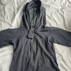 Grå Britney Spears Playboy hoodie  - Grå Britney Spears Playboy hoodie med spets i luvan och över axlarna.