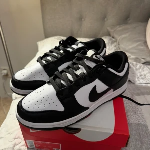 Nike Dunk Low Retro svart/vit 43 - Nike Dunk Low Retro i klassisk svart och vit färg. Skorna har lågt skaft, svart swoosh och snörning. Ovandelen är i skinn med perforerad tåbox för extra andningsförmåga. Perfekta för dig som gillar streetstyle och vill ha en ikonisk sneaker i garderoben.