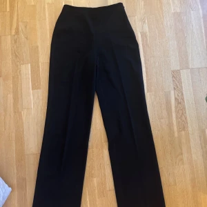 Svarta kostymbyxor från NAKD - Snygga svarta kostymbyxor från NAKD i klassisk rak modell med hög midja och diskret dragkedja i sidan. Byxorna har två fuskfickor bak och är tillverkade i ett slätt tyg som ger en stilren look. Använda fåtal gånger