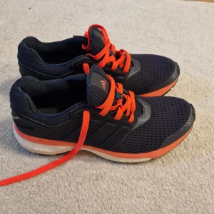 Adidas löparskor med Boost-sula - Snygga Adidas löparskor med marinblå mesh-överdel och rosa snörning. Skorna har en vit och risa Boost-sula för extra komfort och Continental-gummisula för bra grepp. Perfekt för dig som gillar att sticka ut med färg på gymmet eller löprundan.