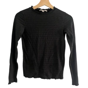 Svart långärmad topp från Garcia - Svart långärmad topp från Garcia med diskret ribbad struktur och vågiga kanter vid hals och ärmslut. Tunn och stretchig, perfekt att styla lager på lager eller som den är. Enkel och stilren design som funkar till allt.