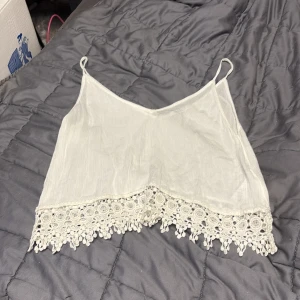 Vit linnetopp med spets från Gina Tricot - Supersöt vit linnetopp från Gina Tricot i storlek 36. Toppen har tunna axelband och en v-ringad hals. Nedtill finns en bred spetskant med detaljerade broderier och hängande spetsdetaljer