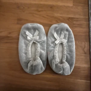 Grå fluffiga tofflor. - Supermysiga grå tofflor i mjukt syntetmaterial, perfekta att glida runt hemma i. De har en rund tå och är dekorerade med en söt rosett framtill. Köpta får typ två år sedan. Ganska bra skick.