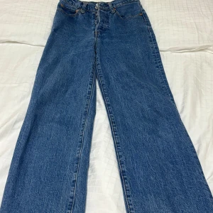 Levi's Ribcage Straight jeans blå W24 - Snygga Levi's Ribcage Straight jeans i klassisk blå tvätt med hög midja och raka ben. Modellen har knäppning med fyra silverfärgade knappar och ikoniska bakfickor med Levi's-lappen. Perfekt för dig som gillar retrovibe och tidlös denimstil.