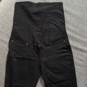 Svarta högmidjade skinny byxor - Svarta gravidbyxor med superhög midja och smal passform. Klassisk femficksdesign och stretchigt material som sitter tajt längs benen. Perfekta för dig som gillar en riktigt hög midja och en clean look.