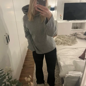 Grå stickad hoodie med huva - Mysig grå stickad hoodie med huva och breda ribbade muddar. Tröjan har en relaxed passform och är perfekt för kyliga dagar. Enkel och stilren design som passar till det mesta.