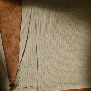 Beige ribbad långkjol - Säljer en beige långkjol med diskreta vertikala ränder och ribbad struktur. Kjolen har en rak passform och en liten slits framtill för extra rörelsefrihet. Perfekt för dig som gillar en stilren och enkel look.