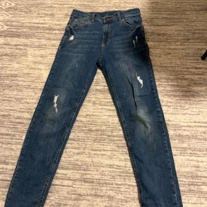 Blå jeans från LC Waikiki - Snygga blå skinny jeans från LC Waikiki med slitna detaljer och klassisk femficksdesign. Jeansen har normalhög midja och är tillverkade i jeansmaterial med gul kontrastsöm. Perfekta för dig som gillar en trendig och avslappnad look.