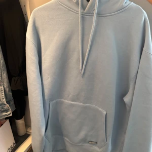 Ljusblå hoodie från Pull&Bear - Säljer en ljusblå hoodie från Pull&Bear i mjuk bomullsmix. Tröjan har huva med snörning, stor magficka och relaxed fit. Perfekt för dig som gillar enkel och clean stil. Pull&Bear-logga på fickan.
