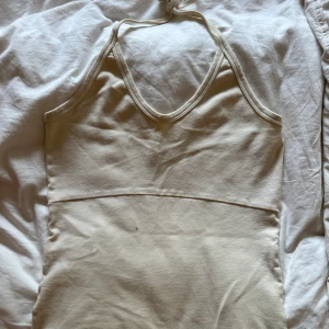 Beige halterneck linnetopp - Säljer en stilren beige linnetopp med halterneck och djup v-ringning. Toppen är ärmlös och har en enkel, clean design som passar perfekt till sommaren. Mjuk och skön mot huden, lätt att matcha med olika outfits.🥰💞