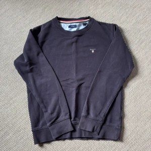 Gant - Mörkblå sweatshirt - En stilren mörkblå sweatshirt från Gant med rund halsringning och diskret logga på bröstet. Tröjan har långa ärmar och ribbade muddar vid ärmslut och nederkant. Perfekt för dig som gillar klassisk och enkel stil.