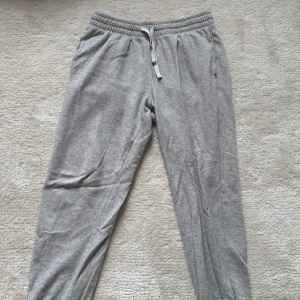 Grå mjukisbyxor från H&M, storlek M - Grå mjukisbyxor från H&M i regular fit med resår och snörning i midjan. Byxorna har muddar vid bensluten och är tillverkade i en mjuk bomullsblandning. Perfekta för chill eller träning. Klassisk och enkel design.