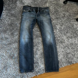 Diesel Safado jeans blå W30 L30 - Snygga blå Diesel Safado jeans med klassisk femficksdesign och raka ben. Jeansen har en cool tvätt med slitningar och är tillverkade i stretchigt denim för extra komfort. Perfekta för dig som gillar en avslappnad men stilren look.