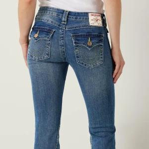 True Religion Joey Low Rise Flare Jeans - Säljer ett par blå True Religion Joey jeans med låg midja och utsvängda bootcut-ben. Klassiska fickor med gul kontrastsöm och logoknappar. Snygg passform och ikonisk etikett bak. Använda ett fåtal gånger och i mycket gott skick! Nypris 1299kr