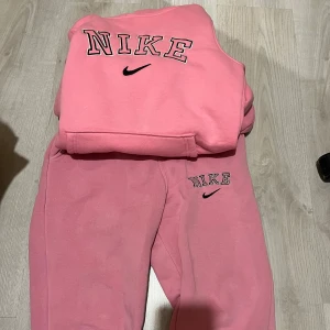  sweatshirt med broderad logo - Säljer en rosa sweatshirt med stor broderad logotyp och svart swoosh framtill. Tröjan har klassisk passform och är gjord i mjuk bomullsmix, perfekt för chill dagar eller när du vill ha en sportig vibe.