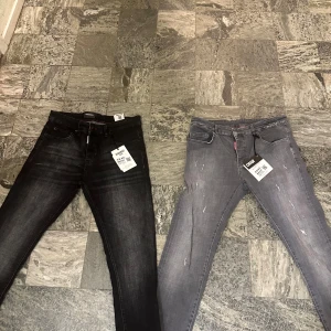 DSQUARED2 jeans i svart och grått - Två par DSQUARED2 jeans, ett par i svart tvätt och ett i grå tvätt med slitningar. Båda har klassisk femficksdesign, röda och svarta DSQUARED2-taggar och röda sömdetaljer vid linningen. Slimmad passform och tillverkade i stretchig bomullsdenim.