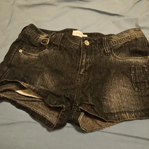 Svarta jeansshorts från NYNY, strl 38 - Snygga svarta jeansshorts från NYNY i 100% bomull. De har råa kanter, coola spänndetaljer vid fickorna och klassisk femficksdesign. Perfekta för dig som gillar en edgy och avslappnad stil. Passar till allt och är superbekväma!