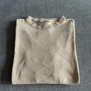 Beige stickad tröja  - Snygg beige stickad tröja från H&M med rund halsringning och ribbade detaljer vid halsen. Perfekt för lager-på-lager och passar till allt. Enkel och stilren design som är lätt att matcha med dina favoritjeans.