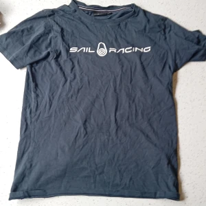 Mörkblå Sail Racing t-shirt - Snygg mörkblå t-shirt från Sail Racing med vit logga tryckt på bröstet och en liten logga i nacken. Klassisk passform och rund halsringning, perfekt till jeans eller shorts. Gjord i mjuk bomull för skön känsla hela dagen.