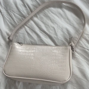 Fin vit handväska - Fin vit handväska med krokopräglad yta och silverfärgad dragkedja. Väskan har en enkel, avlång defekter och ett rymligt svart foder inuti. Har inga dexter och ser helt oanvänd ut.