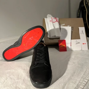 Christian Louboutin svarta sneakers mocka - Svarta sneakers från Christian Louboutin i lyxig mocka med klassisk röd sula och diskret broderad logga på hälen. Skorna har rund tå, svarta skosnören och platt sula. Kommer med originalkartong, dustbag och äkthetskort.