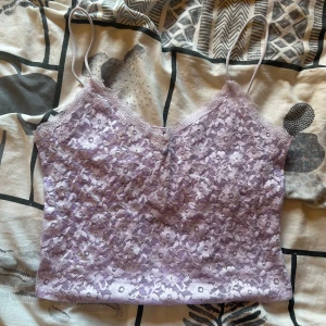 Ljuslila spetsig linnetopp - Säljer en ljuslila linnetopp med tunna axelband och v-ringning. Toppen är täckt av blommig spets och har en feminin, romantisk känsla. Perfekt att styla med jeans eller kjol för en söt look.