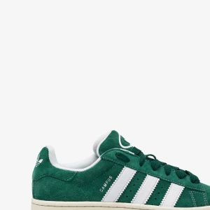Adidas Campus gröna sneakers mocka - Gröna Adidas Campus sneakers i mocka med klassiska vita ränder på sidorna och vit sula. Skorna har snörning och låg profil, perfekt för en avslappnad streetstyle-look. Diskret Campus-tryck i silver på sidan och Adidas-logga på hälen.