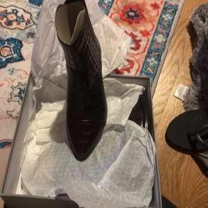 Svarta croc boots med spetsig tå - Säljer ett par svarta boots från Vagabond med croc-präglat mönster och spetsig tå. Skorna har låg klack och är tillverkade i glansigt skinnliknande material. Perfekt för dig som vill ha en edgy och stilren look.