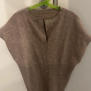 Beige kofta med knappar - Beige kofta i mjukt stickat material med korta ärmar och rund hals. Stängs med knappar framtill och har en enkel, stilren design och blir mer avsmalnad ner till 🙌