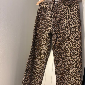 Leopardmönstrade vida  byxor - Säljer ett par snygga byxor med leopardmönster i bruna och beige toner. Byxorna har vid passform och klassisk femficksdesign. Perfekta för dig som vill sticka ut med ett djurmönster och skapa en cool look.