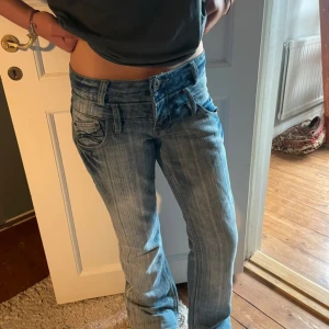 Lågmidjade bootcut jeans  - Säljer ett par lågmidjade bootcut jeans i ljusblå tvätt med snygga slitningar och dekorativa sömmar på bakfickorna. Jeansen har klassisk femficksdesign, bälteshällor och dragkedjegylf. Perfekta för dig som gillar en avslappnad och trendig look, säljer för att dem var för små för mig💕