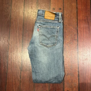 Levi's 511 ljusblå jeans W31 L32 - Säljer ett par Levi's 511 jeans i ljusblå tvätt med klassisk femficksdesign och snygga slitningar. Jeansen har normal passform med smalare ben och är tillverkade i mjukt denimtyg. Två fläckar på höger ben, se sista bilden. 