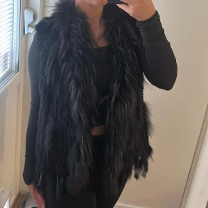 Svart fluffig pälsväst - Säljer en svart pälsväst med lång, fluffig päls och öppen front. 