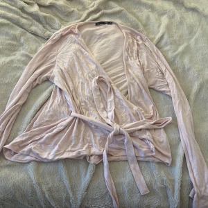 Ljusrosa omlottkofta med knytband - Supersöt ljusrosa omlottkofta från Lager 157 med långa ärmar och knytband i midjan. Koftan är tunn och mjuk och har kommit till användning 1 gång! 💗Storleken fungerar bra som L och XL