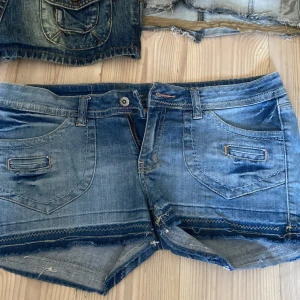 Blå jeansshorts från Fantum - Snygga blå jeansshorts från Fantum med klassisk femficksdesign, slitna detaljer och rå kant nedtill. Shortsen har synliga sömmar i kontrastfärg och knappstängning fram. Insidan av midjan har ett blommigt tyg för extra stilpoäng.