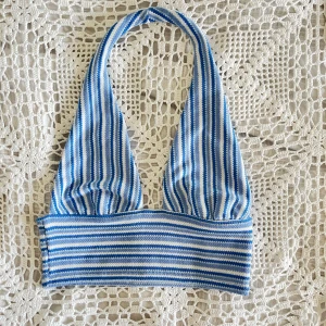 Blåvit halternecktopp - Supersnygg halternecktopp i blått och vitt med randigt mönster. Halterneck-modell med bred resår under bysten och mjukt, stretchigt material. Utsidan är stickad och insidan har ett slätt, ljusblått foder. Perfekta sommartoppen!